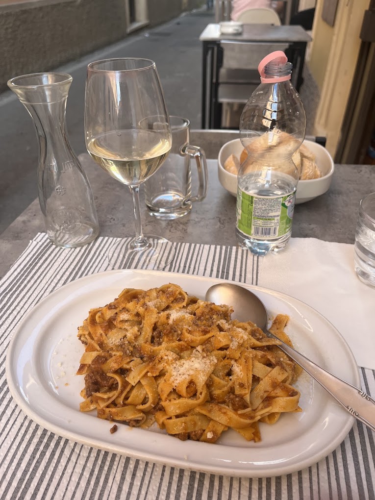 Tagliatelle al ragù con un calice di vino bianco, servite all'aperto